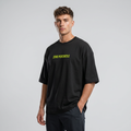 A man wearing a black oversized t-shirt with 'ZERO PERCENTILE' printed in neon yellow across the chest, paired with dark gray pants, against a light gray studio background.